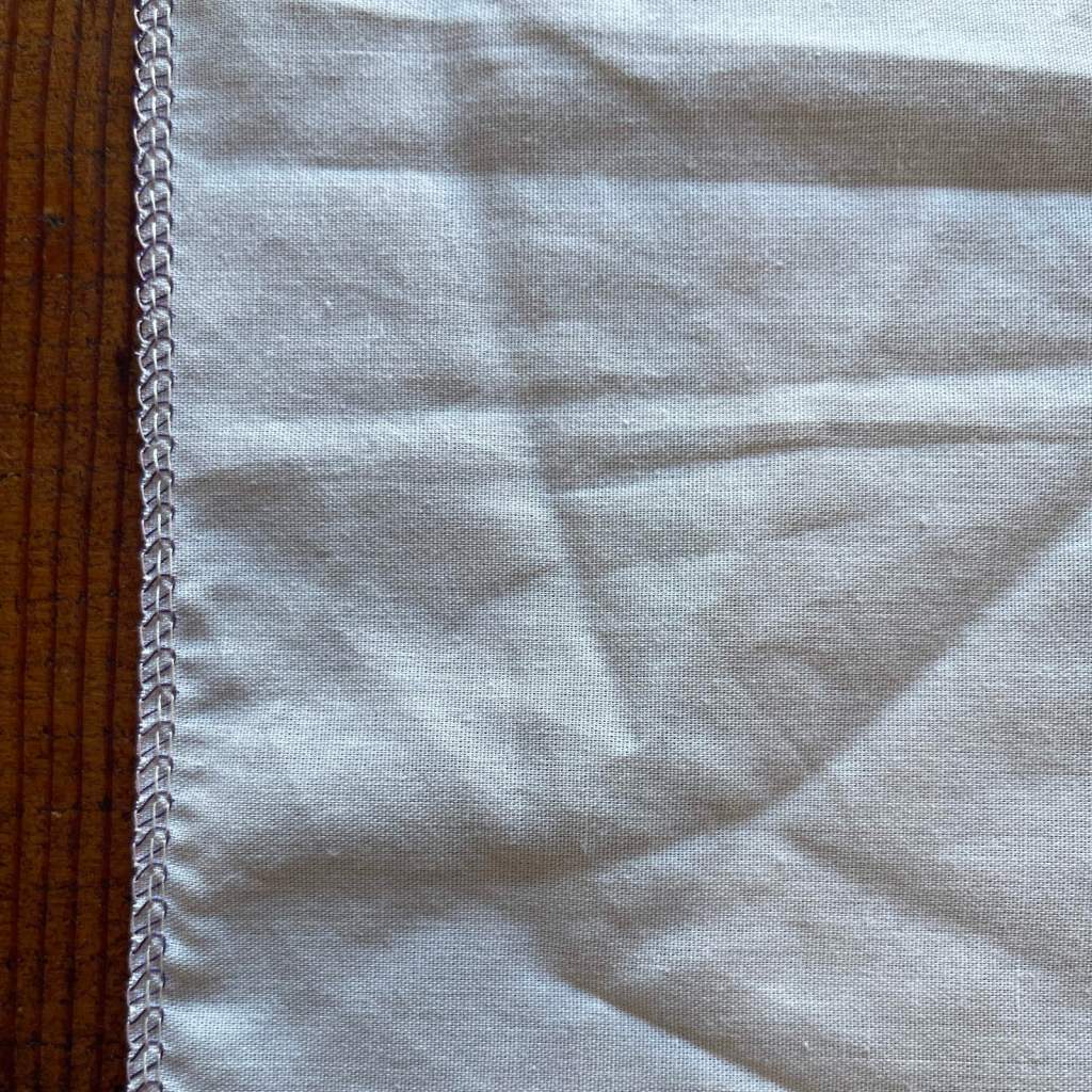 The edge of a white piece of fabric is finished with a serged stitch